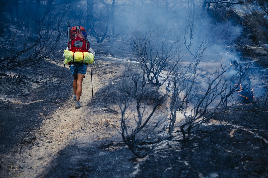 Woman hikes through burning field with a red backpack